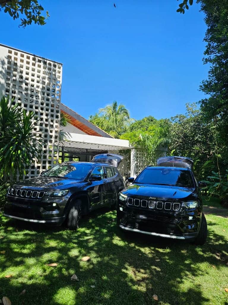 Dois Jeep Compass com porta-malas abertos prontos para receptivo empresarial em jardim tropical