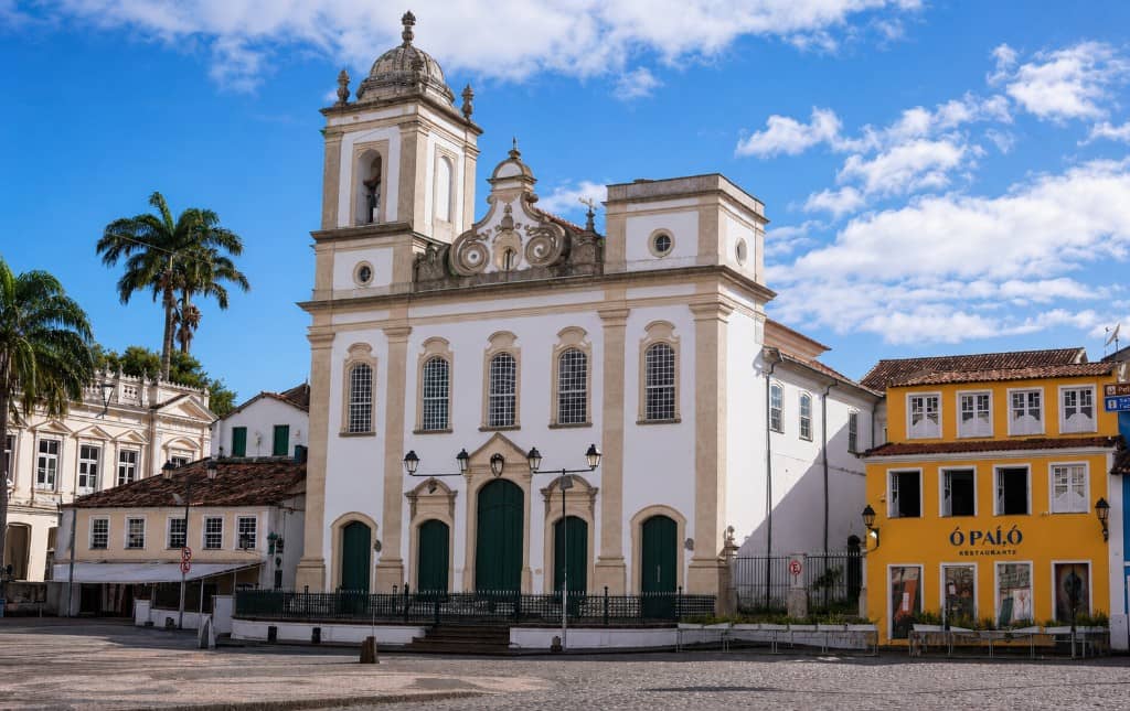 Largo do Pelourinho em Salvador, com igreja colonial branca e casarão amarelo