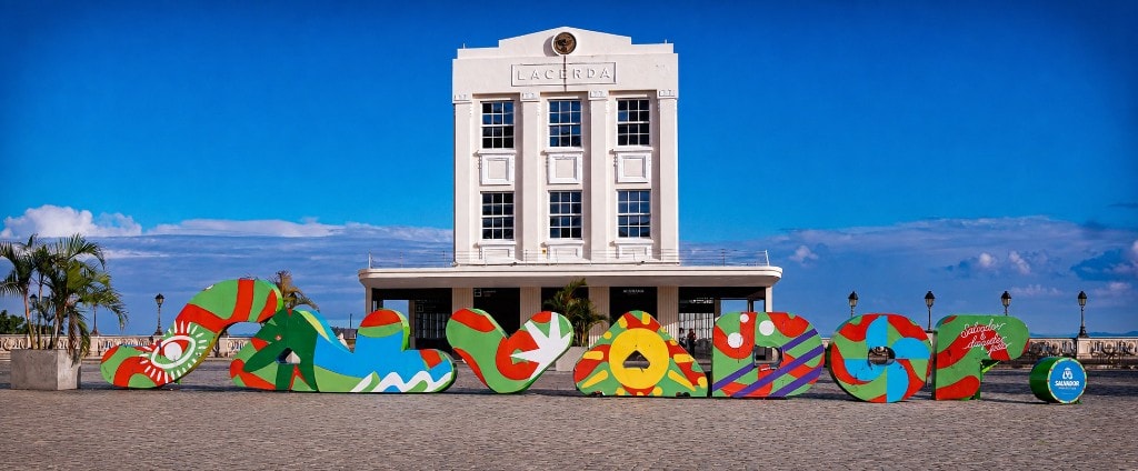 Letreiro colorido SALVADOR na Praça Tomé de Sousa, com o Elevador Lacerda ao fundo